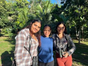 Three students from University of Belize in the forest with binoculars