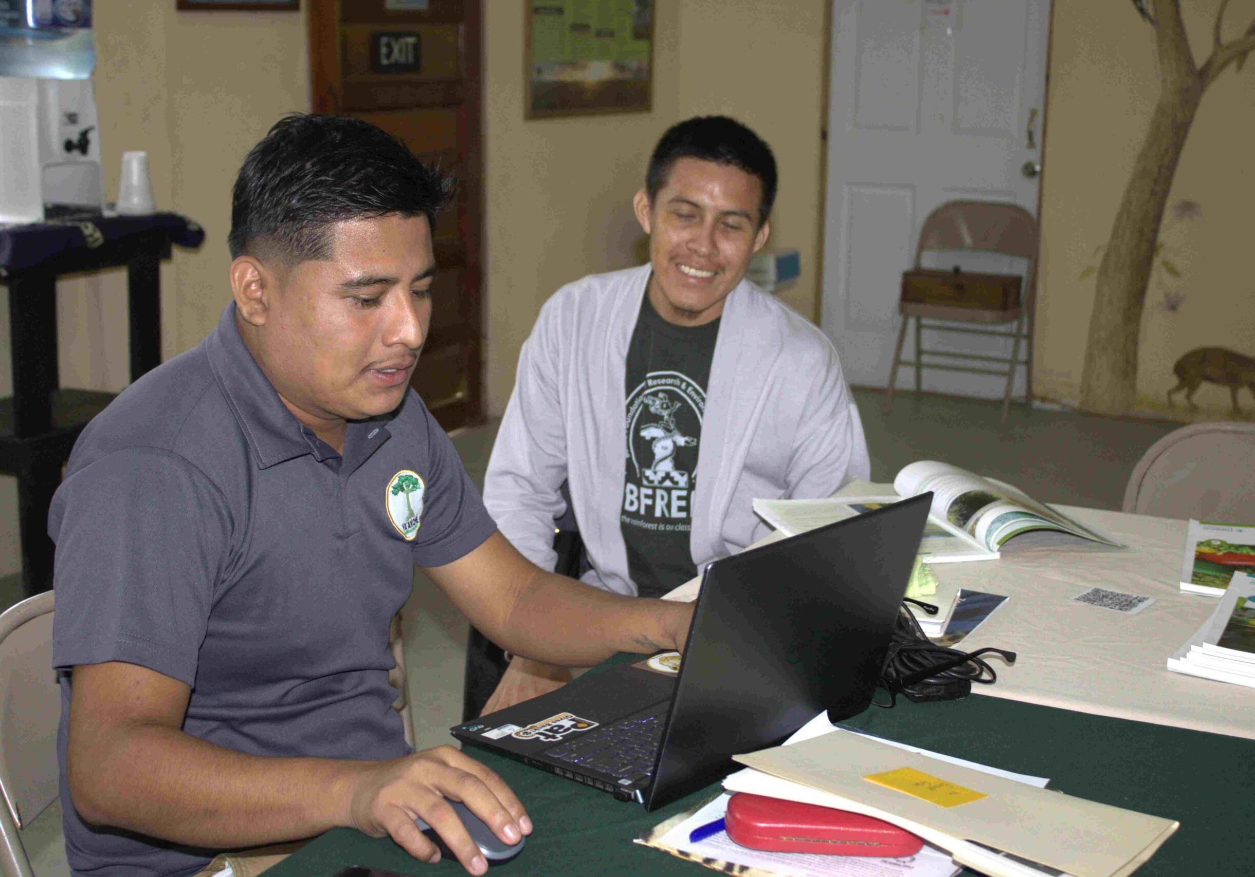 Young man smiles and looks over the shoulder of another man working on a computer