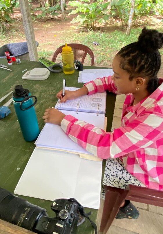 female writing in a notebook on a table outside