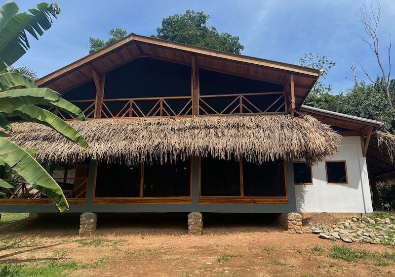 The Commons at BFREE A rustic A-frame building in the Belizean Rainforest at BFREE with a natural thatch awning and decorative wood balancony.